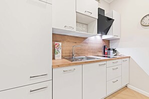 A modern kitchen with white cabinets, a wooden countertop, a stainless steel sink, and a black range hood. - Kaiser Apartment 2BR | Metro | Kitchen | Central (Wien)