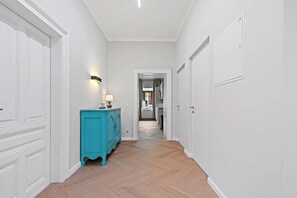 Un couloir aux murs blancs, doté d’un parquet en chevrons, d’une armoire de couleur turquoise et d’une porte au fond.