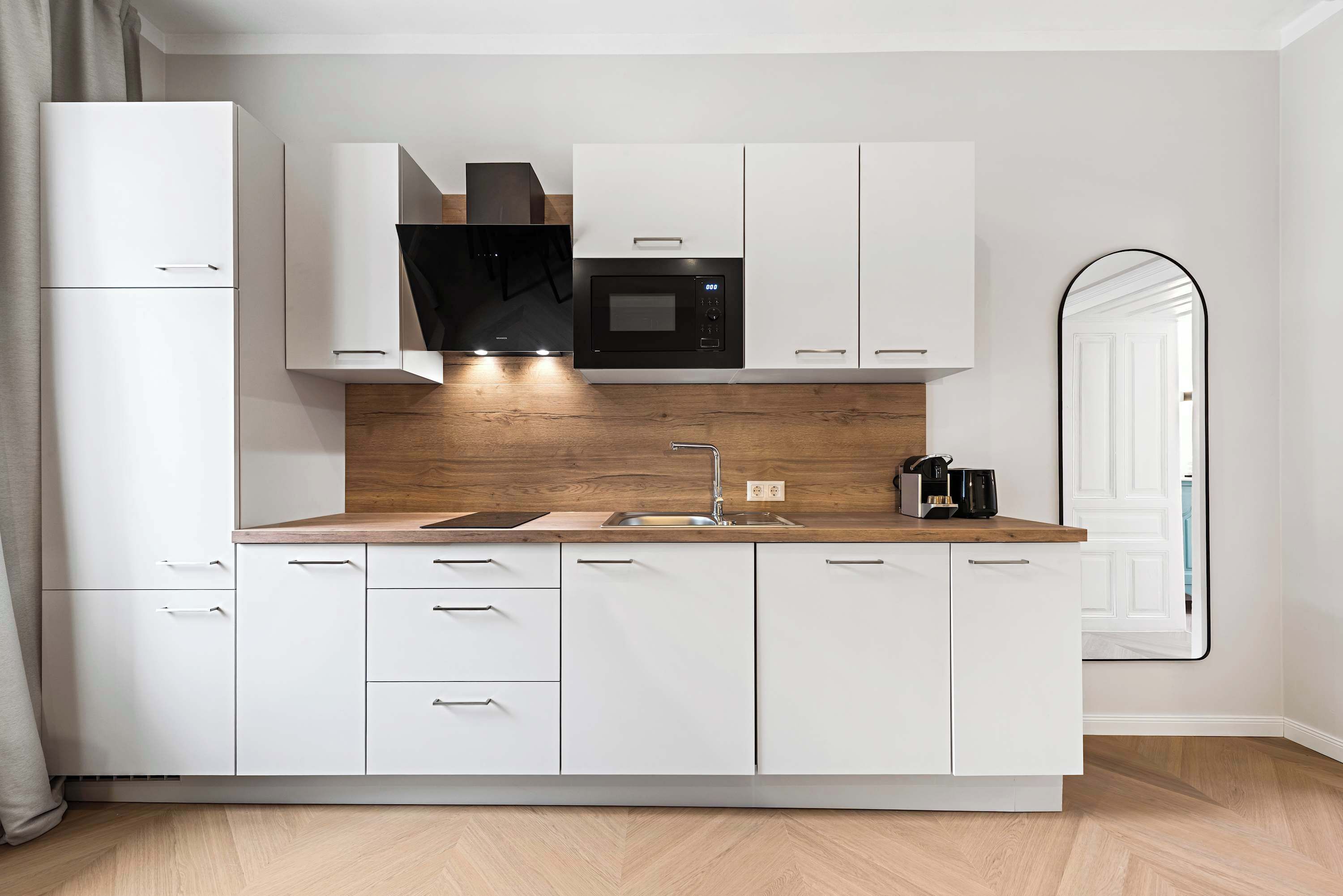 A modern kitchen with white cabinetry, a wooden countertop, a built-in microwave, and a sink.