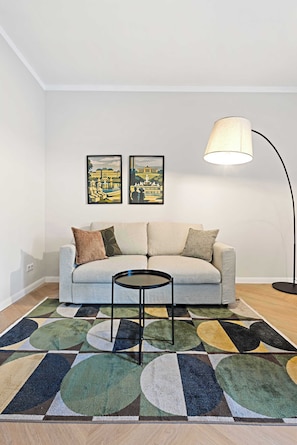Ein Wohnzimmer mit einer Couch, einem Couchtisch, einer Stehlampe und zwei gerahmten Bildern an der Wand.