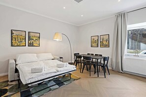 A hotel room with a bed, a dining table with chairs, a lamp, and artwork on the walls. - Kaiser Apartment | Comfort | Kitchen | Central (Wien)