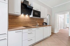 A modern kitchen with white cabinetry, a wooden countertop, a built-in microwave, and a stainless steel sink. - Kaiser Apartment | Comfort | Kitchen | Central (Wien)
