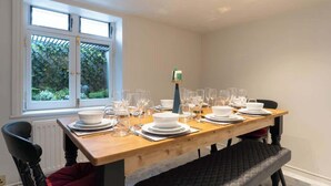 Un coin repas avec une table en bois dressée pour six personnes, une fenêtre donnant sur un paysage verdoyant et un radiateur placé sous la fenêtre.