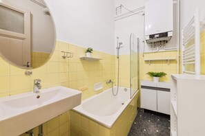 A bathroom with yellow tiles, a white sink, a bathtub, a mirror, and a shower. - Stylish 3BR Apt. | Central | Kitchen | Balcony (Wien)