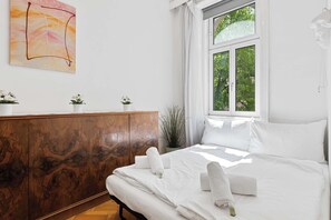 A hotel room with a bed, a wooden wardrobe, a window with a view of trees, and a wall-mounted abstract painting. - Stylish 3BR Apt. | Central | Kitchen | Balcony (Wien)