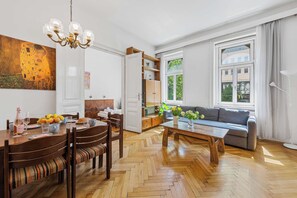 A modern living room with a dining area, a sofa, a coffee table, and a painting on the wall. - Stylish 3BR Apt. | Central | Kitchen | Balcony (Wien)