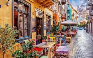 Eine enge Straße mit Außenbestuhlung, einem Café und Häusern mit Balkonen.