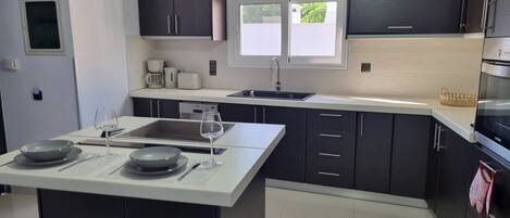 A modern kitchen with dark cabinets, a white countertop, a built-in oven, and a window providing natural light.