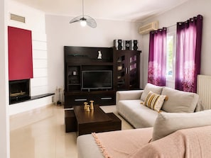 Ein modernes Wohnzimmer mit Kamin, Flachbildfernseher, dunklem Unterhaltungsschrank und einer Couch mit Kissen.