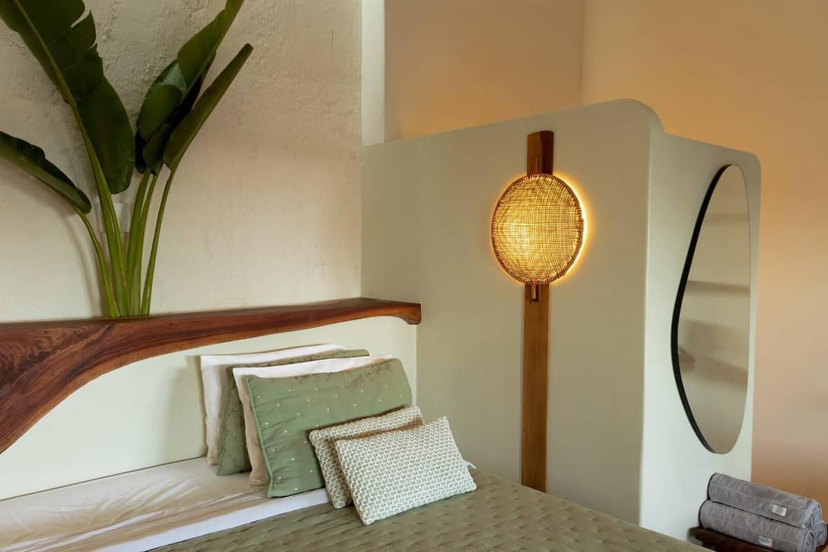 Un dormitorio con cabecera de madera, un espejo grande, una lámpara de pared y una planta en maceta.