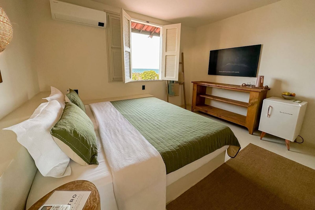 Un dormitorio con cama, televisor, un refrigerador pequeño y una ventana con persianas.