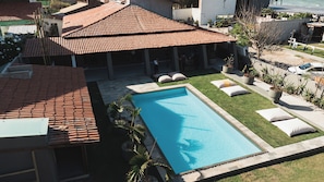 Una piscina con techo de baldosas, un área verde con sillones de descanso y vistas a edificios cercanos.