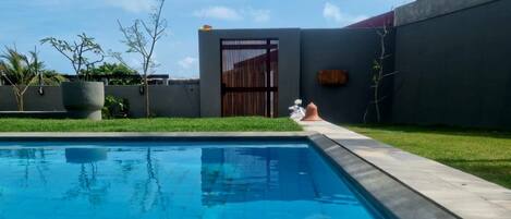 A swimming pool with a clear blue water surface, surrounded by a concrete deck.