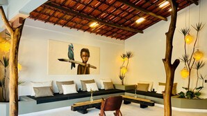 A modern lounge area with a wooden ceiling, a sofa set, a rocking chair, and decorative plants.
