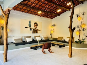 Un área de estar moderna con techo de madera, un conjunto de sofás, un sillón mecededor y plantas decorativas.
