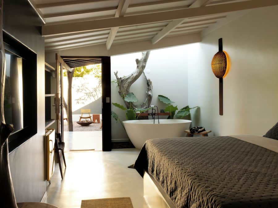 A modern bedroom with a large bed, a bathtub, and a view of a garden.