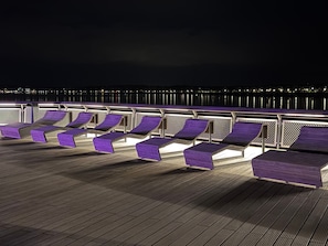 A deck with multiple lounge chairs and a railing, overlooking a body of water at night. - WahlHeimat Haffkrug - Just a few steps from the sea (Scharbeutz)