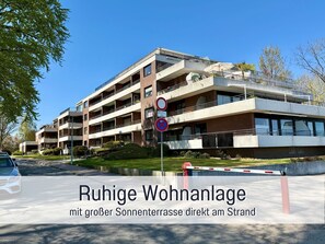 Un edificio residenziale a più piani con balconi, un cancello d'ingresso e cielo sereno.