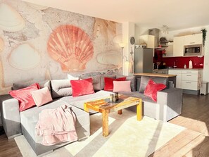A modern living room with a grey sofa, red and grey cushions, a wooden coffee table, and a large wall mural. - WahlHeimat Haffkrug - Just a few steps from the sea (Scharbeutz)