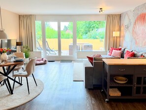 A modern living room with a dining area, a sofa set, a coffee table, a TV, and a view of a garden through large sliding doors. - WahlHeimat Haffkrug - Just a few steps from the sea (Scharbeutz)