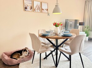 Zona pranzo con tavolo rotondo, sedie, cuccia per cane, decorazione a stella marina e televisore.