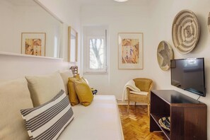 Ein Wohnzimmer mit einer Couch, einem Sessel, einem Fernseher und Kunstwerken an den Wänden.