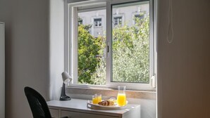 Et lille skrivebord med stol, lampe og bakke med croissanter og appelsinjuice ved et vindue.