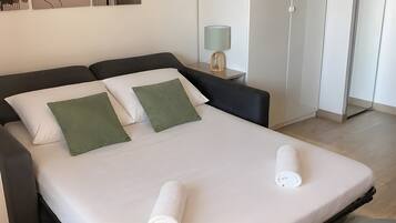 A neatly made bed with pillows, a bedside table with a lamp, a green chair, and artwork on the wall.