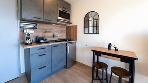 Eine moderne Küche mit grauen Schränken, einem eingebauten Backofen, einer Mikrowelle und einem Spülbecken. Ein Holztisch mit zwei Barhocker und ein dekorativer Spiegel sind an der Wand angebracht.