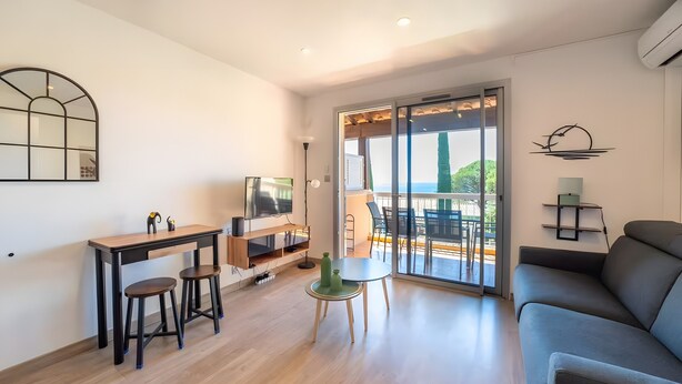Ein modernes Wohnzimmer mit Sofa, Fernseher, Esstisch mit Hocker und Balkon mit Aussicht.