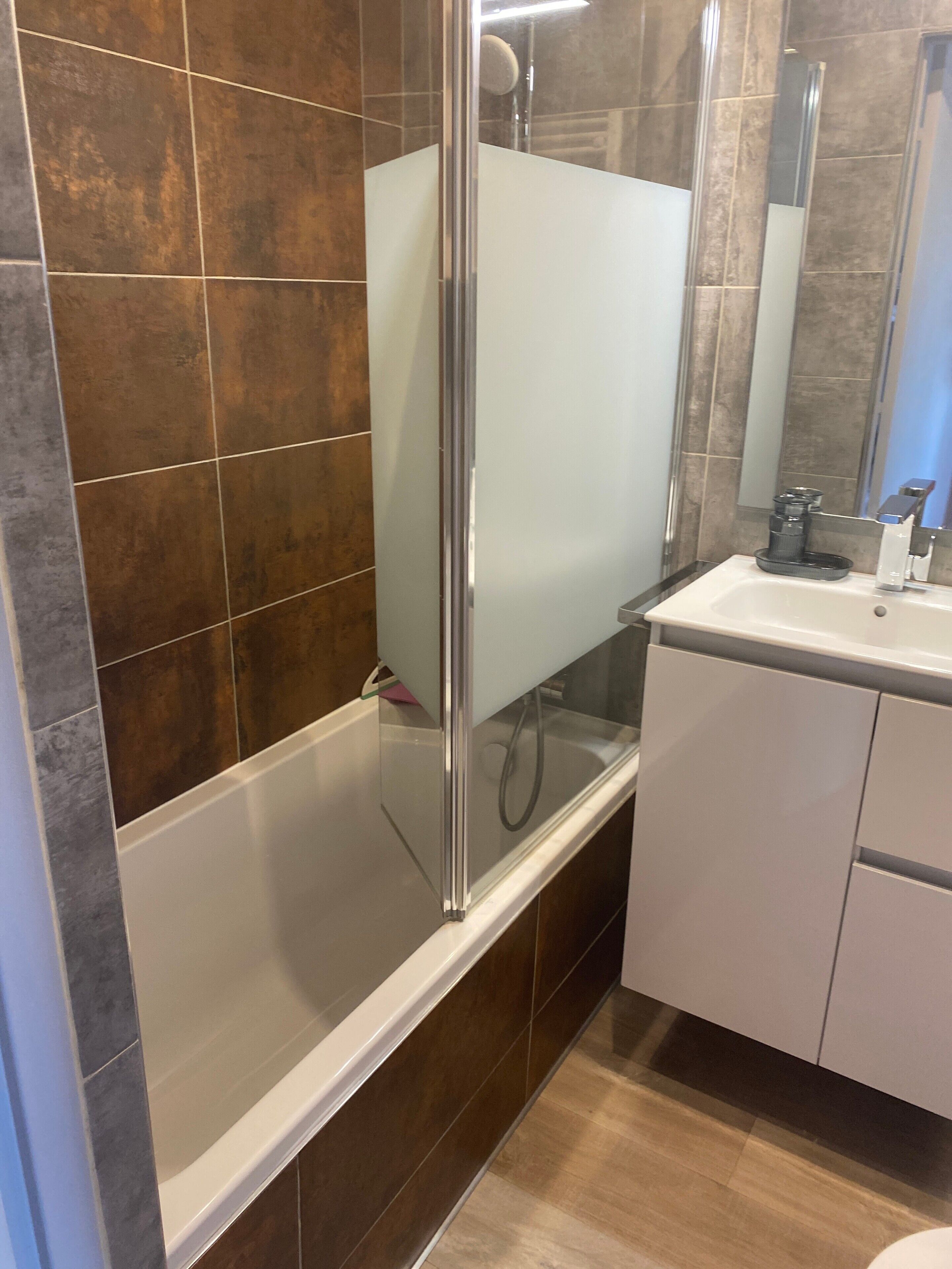 A modern bathroom with a glass-enclosed shower, a white sink, and a mirror above it.
