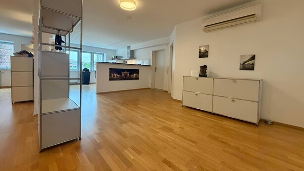 Une pièce spacieuse avec un plancher en bois, une armoire blanche, une étagère en métal et, au fond, un coin cuisine.