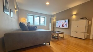 Un salon moderne avec un canapé gris, un téléviseur, une petite table et un meuble blanc.