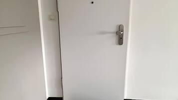 Une porte blanche fermée, dotée d’une poignée et d’une petite plaque de serrure, un paillasson noir sur lequel est inscrit le mot « bienvenue », et un sol carrelé.