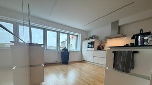 Une cuisine moderne avec des meubles blancs, une grande fenêtre et une vue sur les bâtiments environnants.