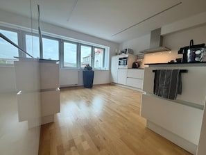 Une cuisine moderne avec des meubles blancs, une grande fenêtre et une vue sur les bâtiments environnants.