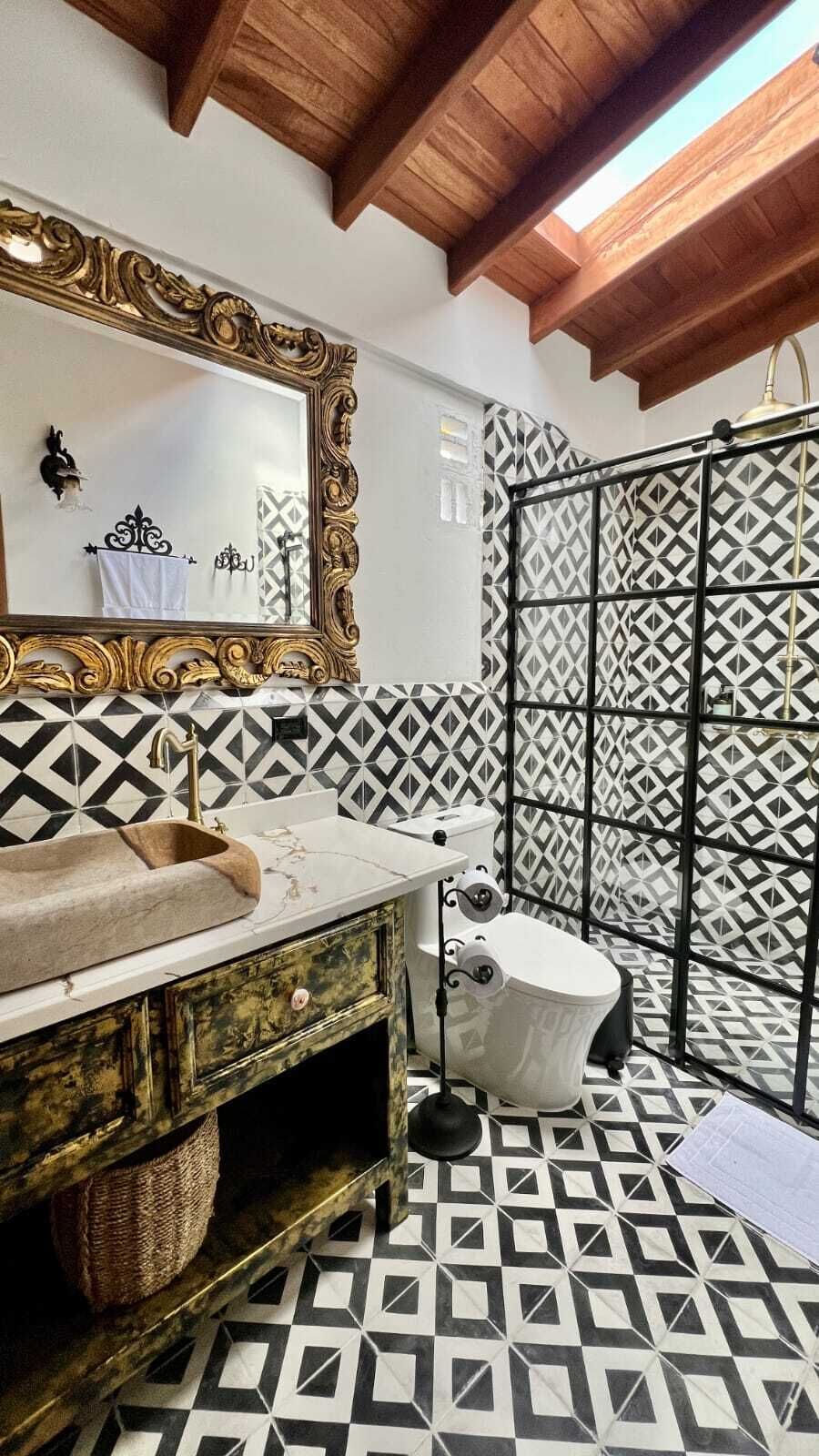 Un baño con piso de estampado geométrico, un lavamanos con espejo decorativo, un inodoro y una zona de ducha.