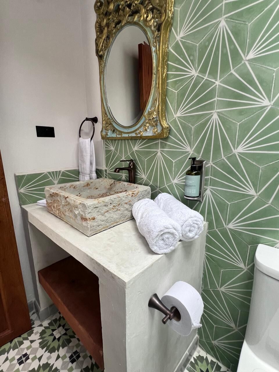 Ein Badezimmer mit Marmorwaschbecken, einem goldfarbenen Spiegelrahmen, einem Handtuchhalter und einem Toilettenpapierhalter.