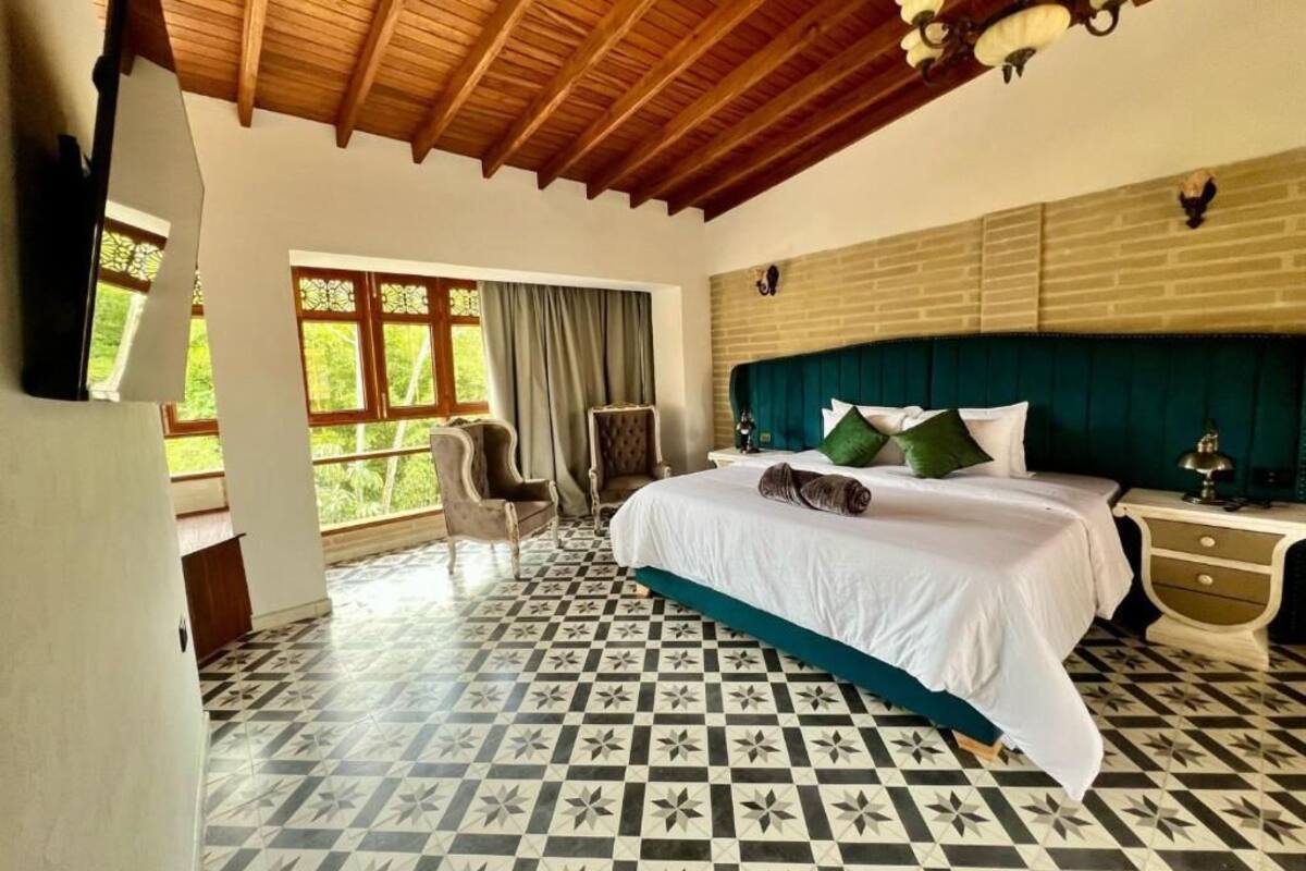 Un dormitorio con piso a cuadros, cama con ropa de cama verde y blanca, techo de madera y pared de ladrillo.