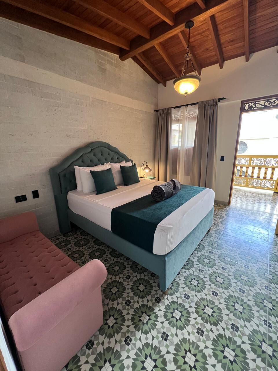 Un dormitorio con cama, una silla, un balcón y un suelo estampado.