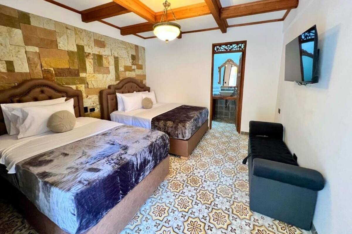 Una habitación con dos camas, televisión, techo de madera y piso con diseño.