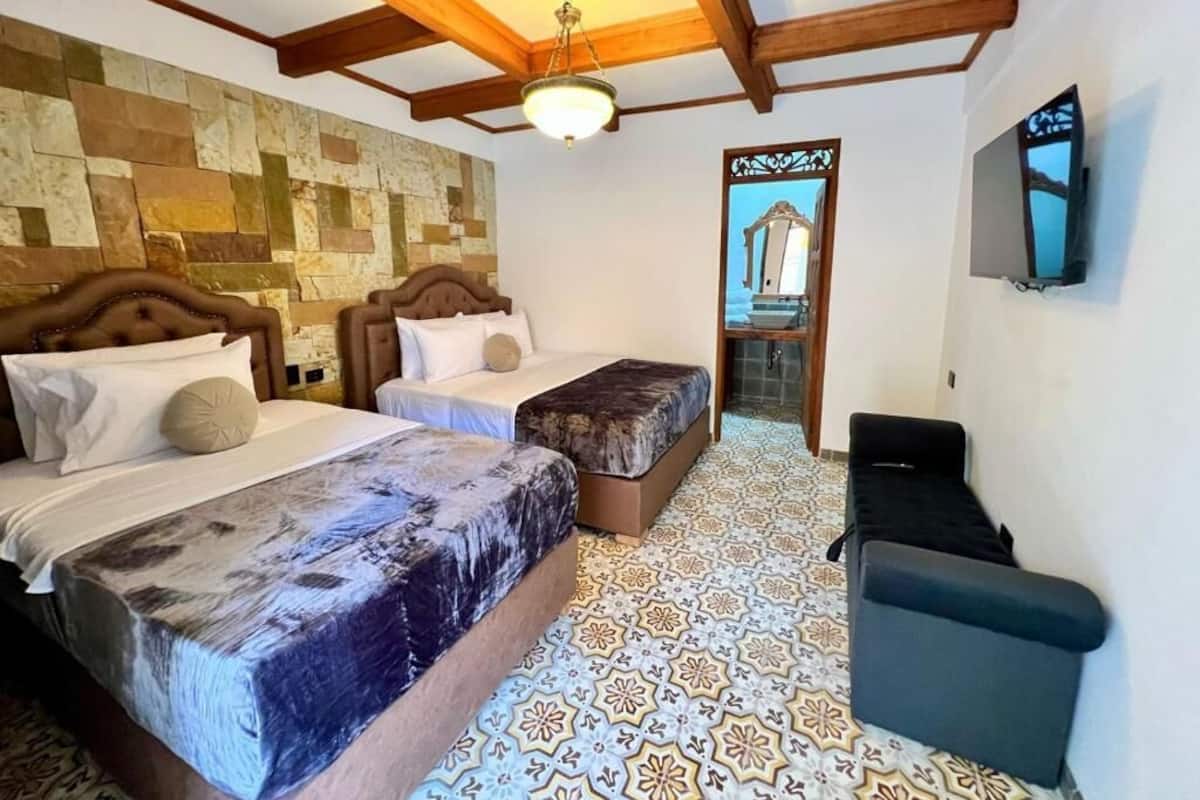 A room with two beds, a TV, a wooden ceiling, and a patterned floor.