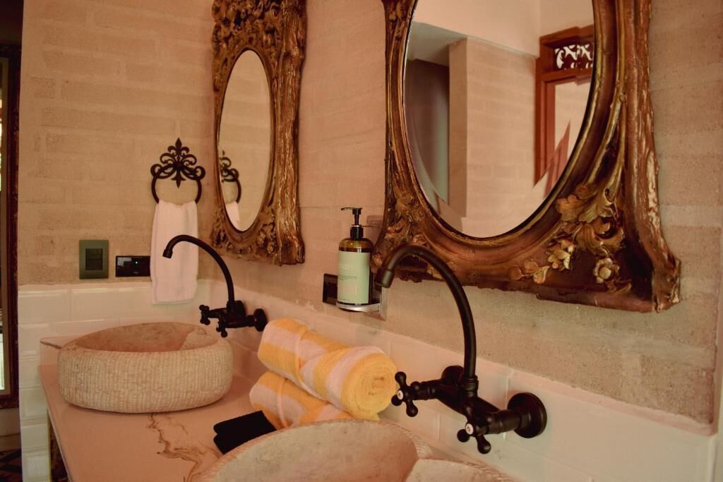 A bathroom with a round sink, two mirrors, and a bottle of soap.