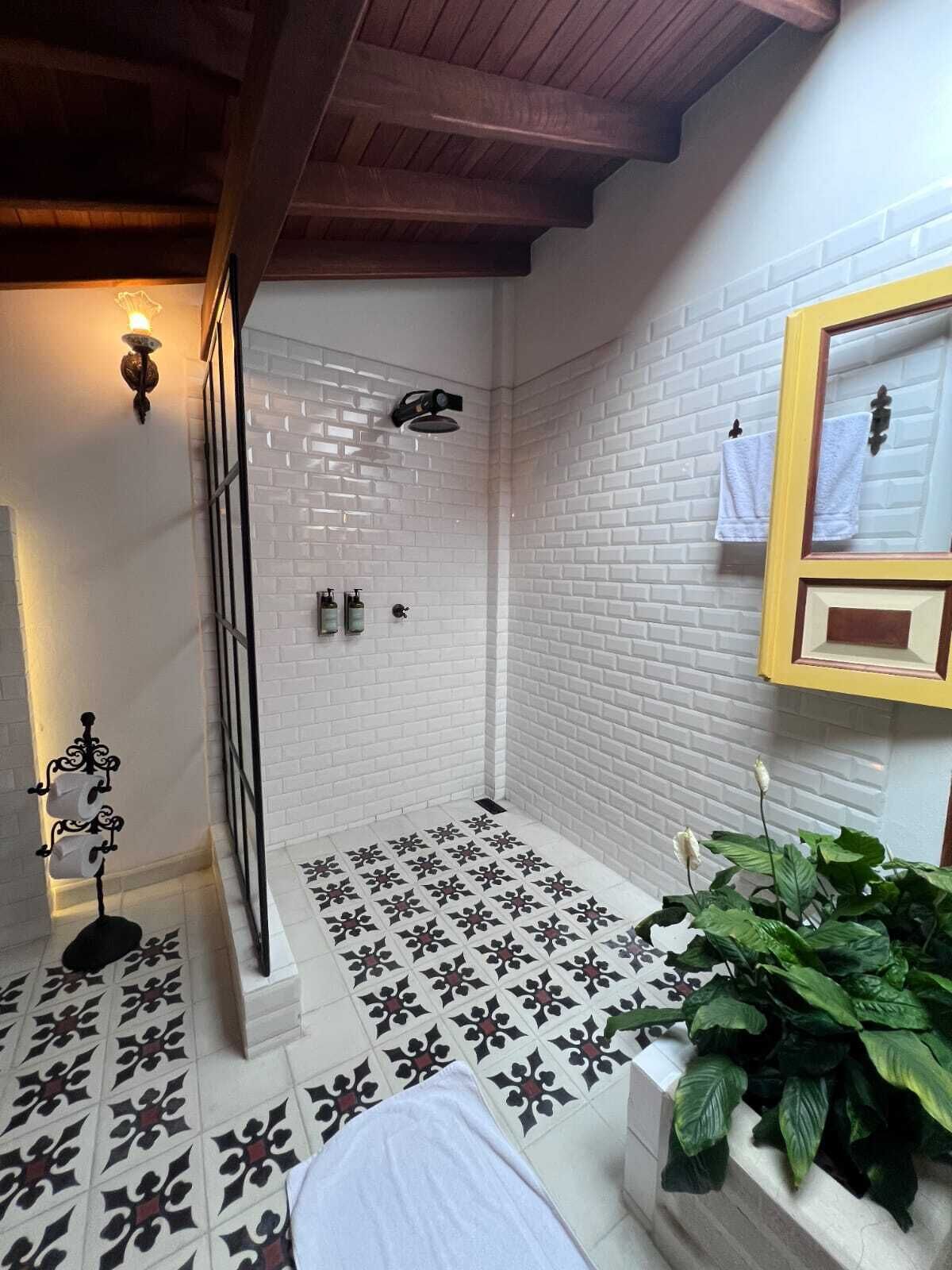A shower with white brick walls and a tiled floor, a wooden ceiling, and a mirror with a yellow frame.