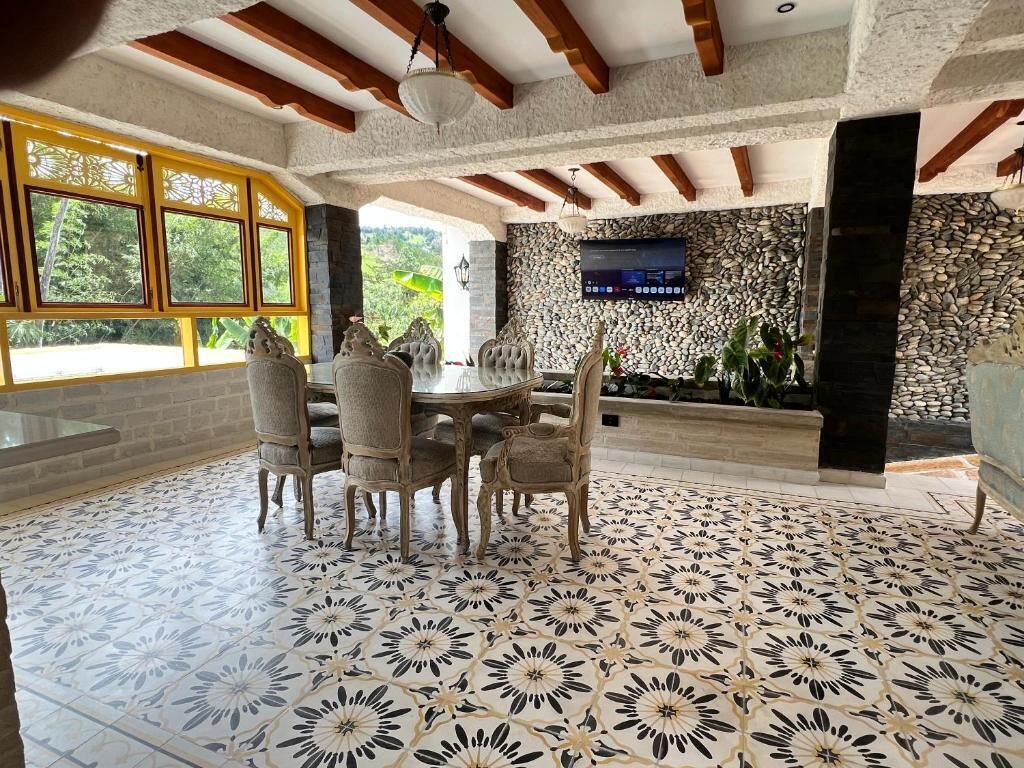 A dining area with a stone wall, a TV mounted on the wall, and a patterned floor.