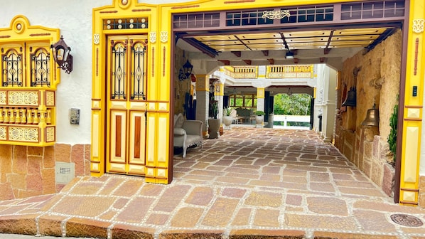 A yellow entrance with a stone floor, a white wall, and a balcony with yellow railings.