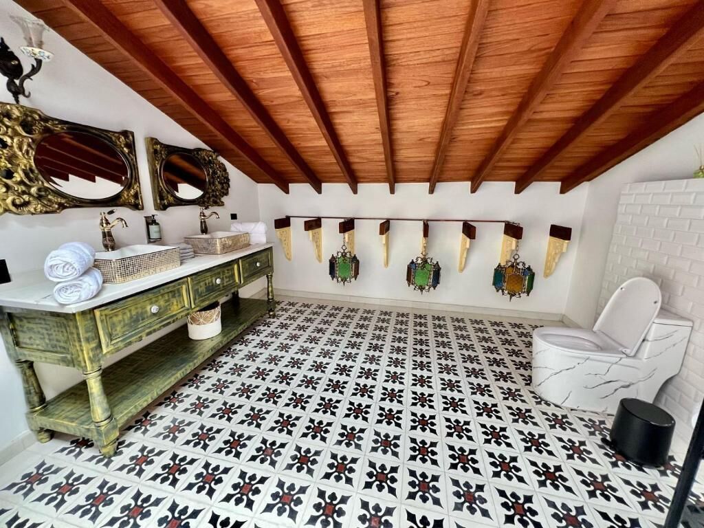Een badkamer met een vloertekening, een wit toilet, een wastafel met spiegel en een hanglamp.