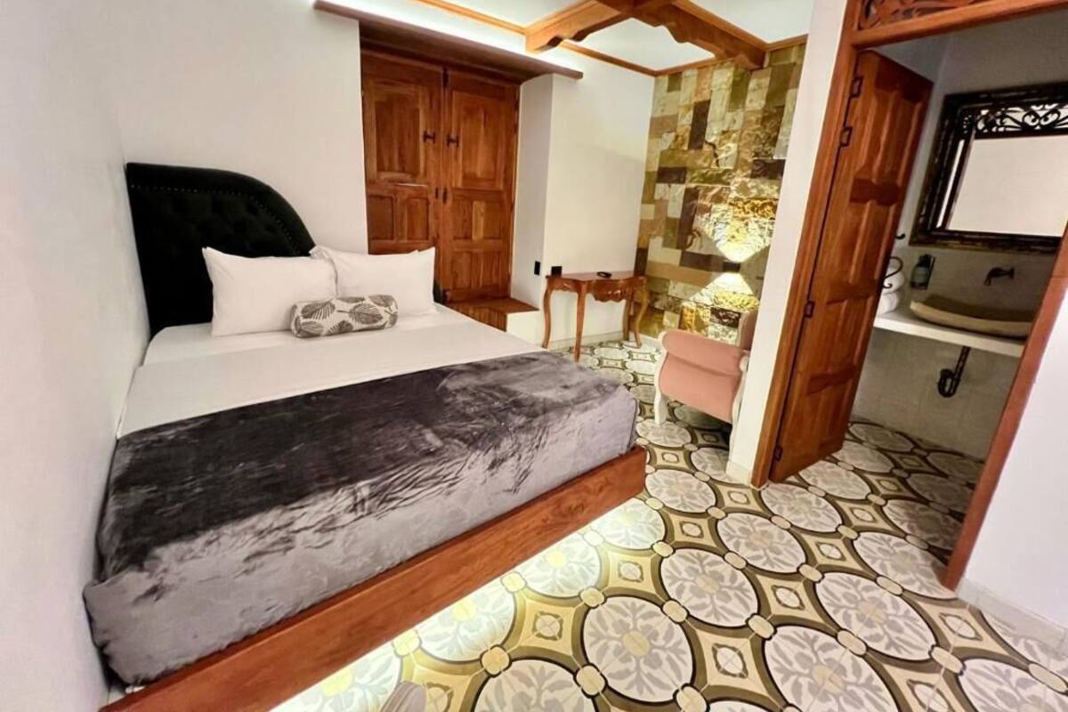 Un dormitorio con cama, armario de madera, una mesita y un baño con espejo y lavamanos.