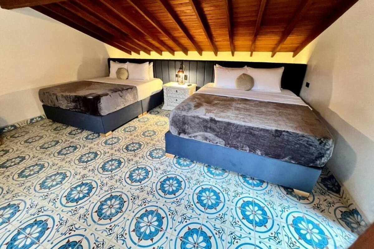 Una habitación con dos camas, una mesita de noche y baldosas de suelo con diseño.