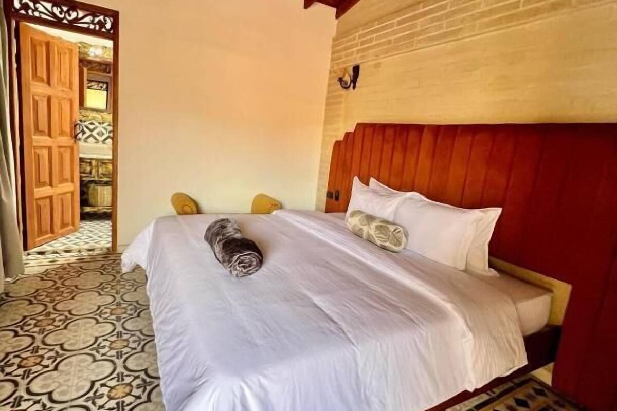 Una habitación con cama, suelo estampado y techo de madera.